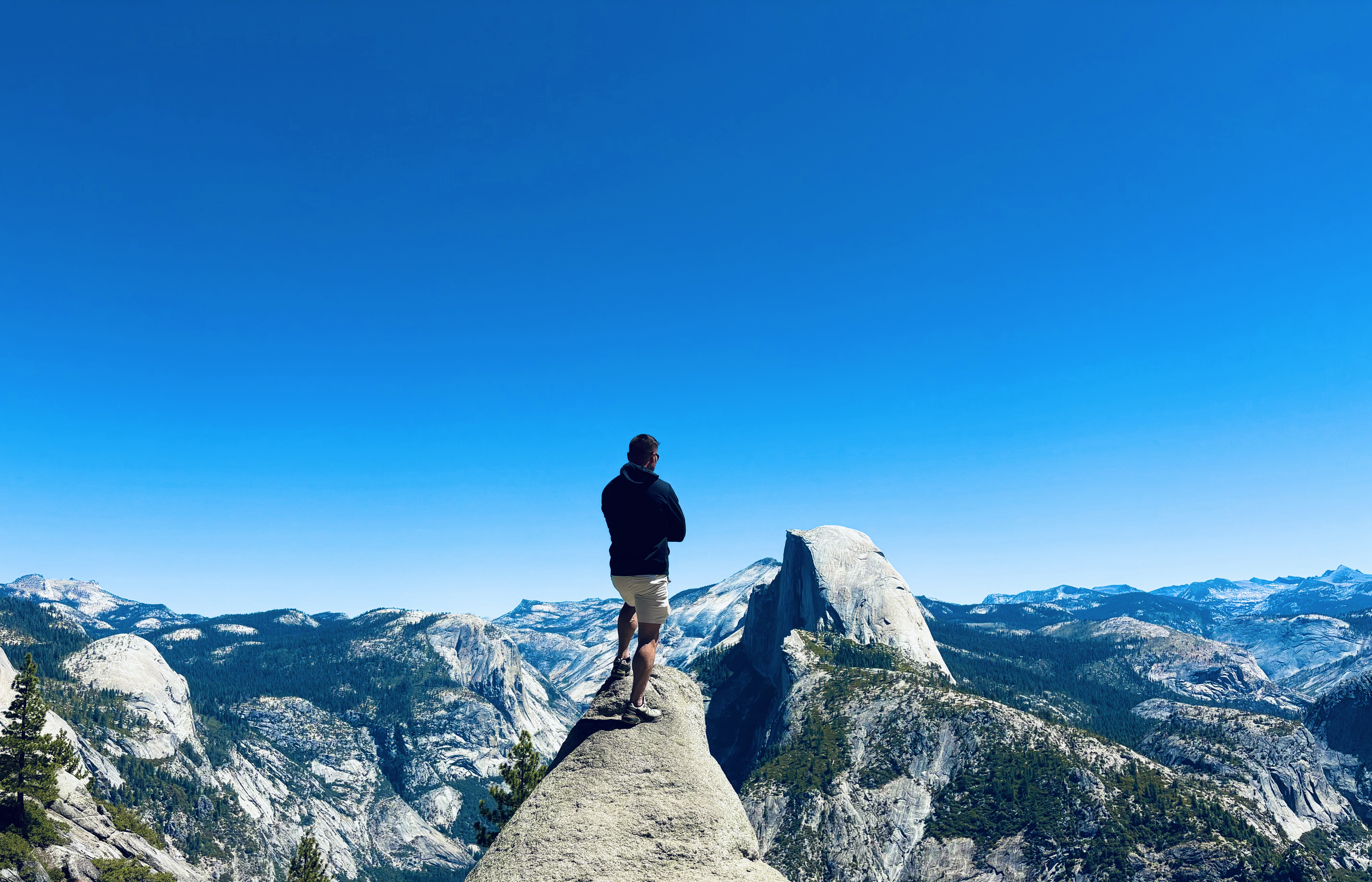 Will Duvall standing on a rock outcropping at Yosemite, overlooking Half Dome and a vast mountain landscape under a deep blue sky — a man at the edge of the world, walking his own way.